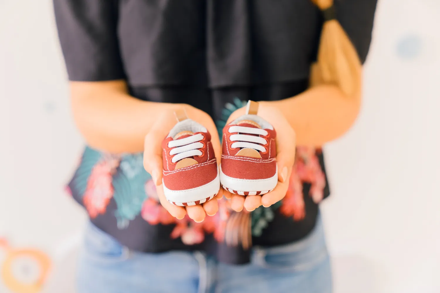 Un par de zapatos rojos para bebé con cordones blancos, sostenidos por una persona, en un ambiente iluminado y acogedor.