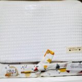 Funda de tela blanca con textura, decorada con un lazo de estampado colorido, etiquetada como Creaciones Nunai. Ideal para proteger y presentar productos, fabricada en 100% algodón y material plástico ecológico EVA. Precio visible de $24.95.