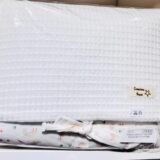 Manta blanca texturizada y manta con diseño de arcoíris, empaquetadas juntas. Ideal para bebés, con etiqueta de Creacions Nunal y precio de 24.95.